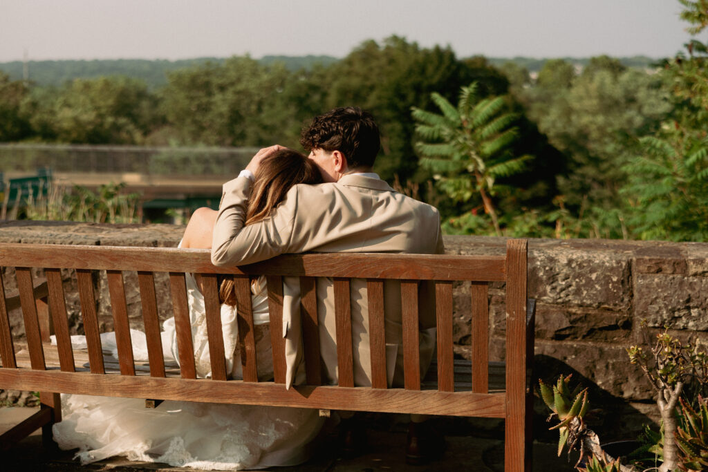 A bride and groom looking out to the forest sitting together on a bench.