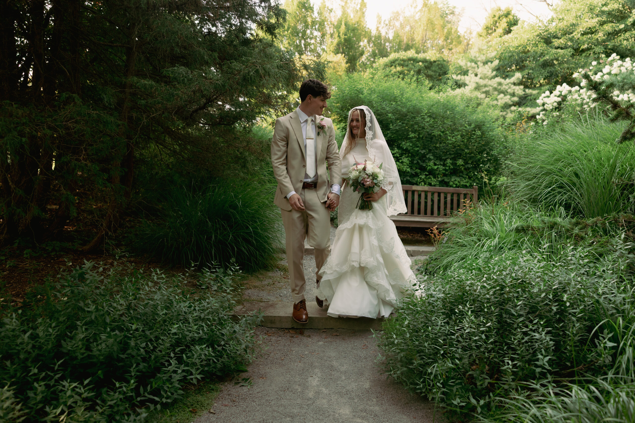 A bride and groom walking through a garden of large green plants.