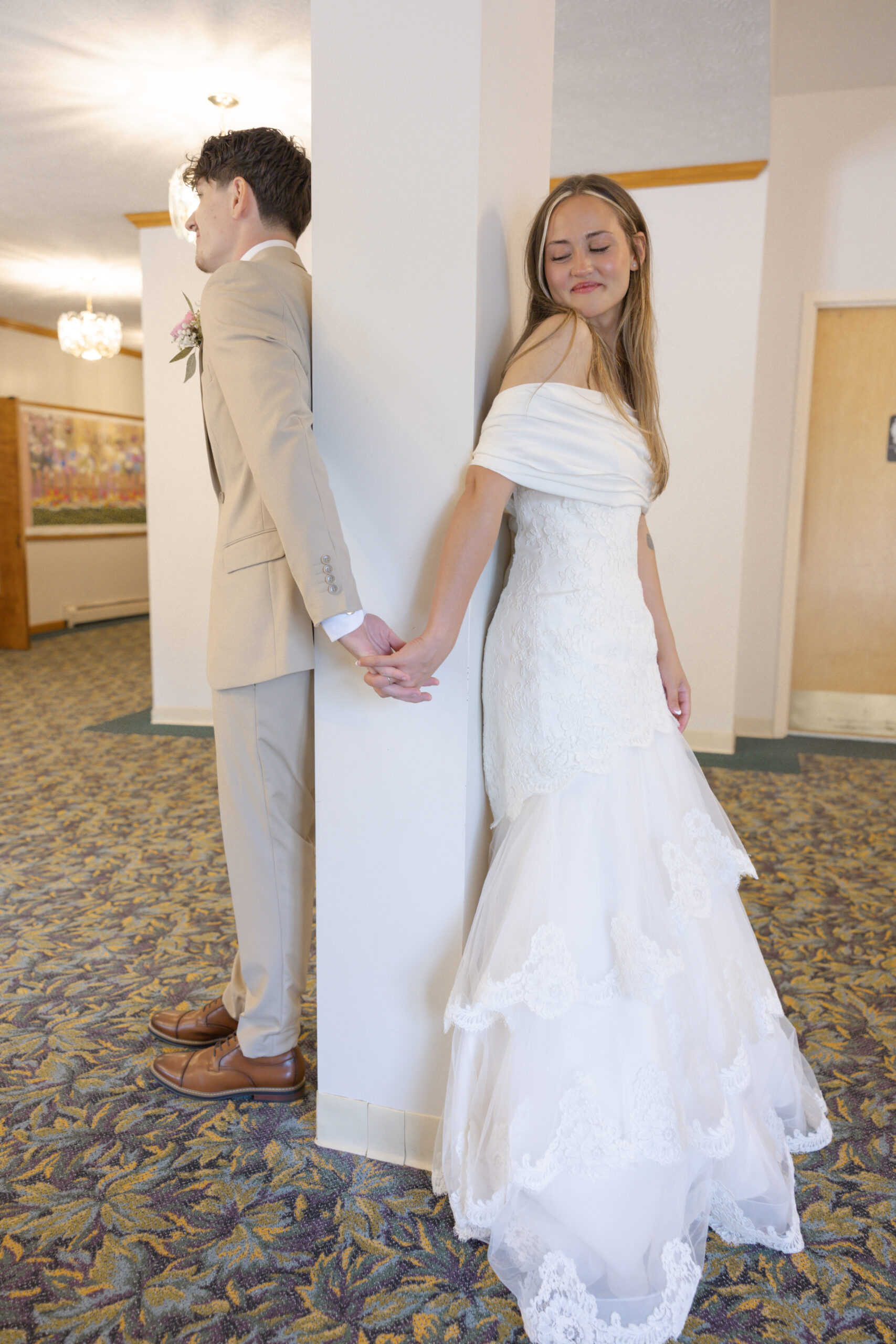 A bride and groom holding hands opposite side of a pole.