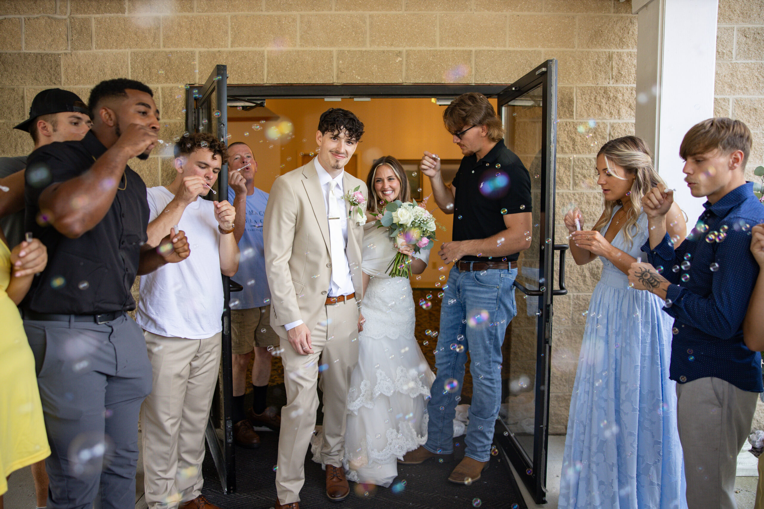 A bride and groom walking down an aisle of family and friends as bubbles are being blown at them.
