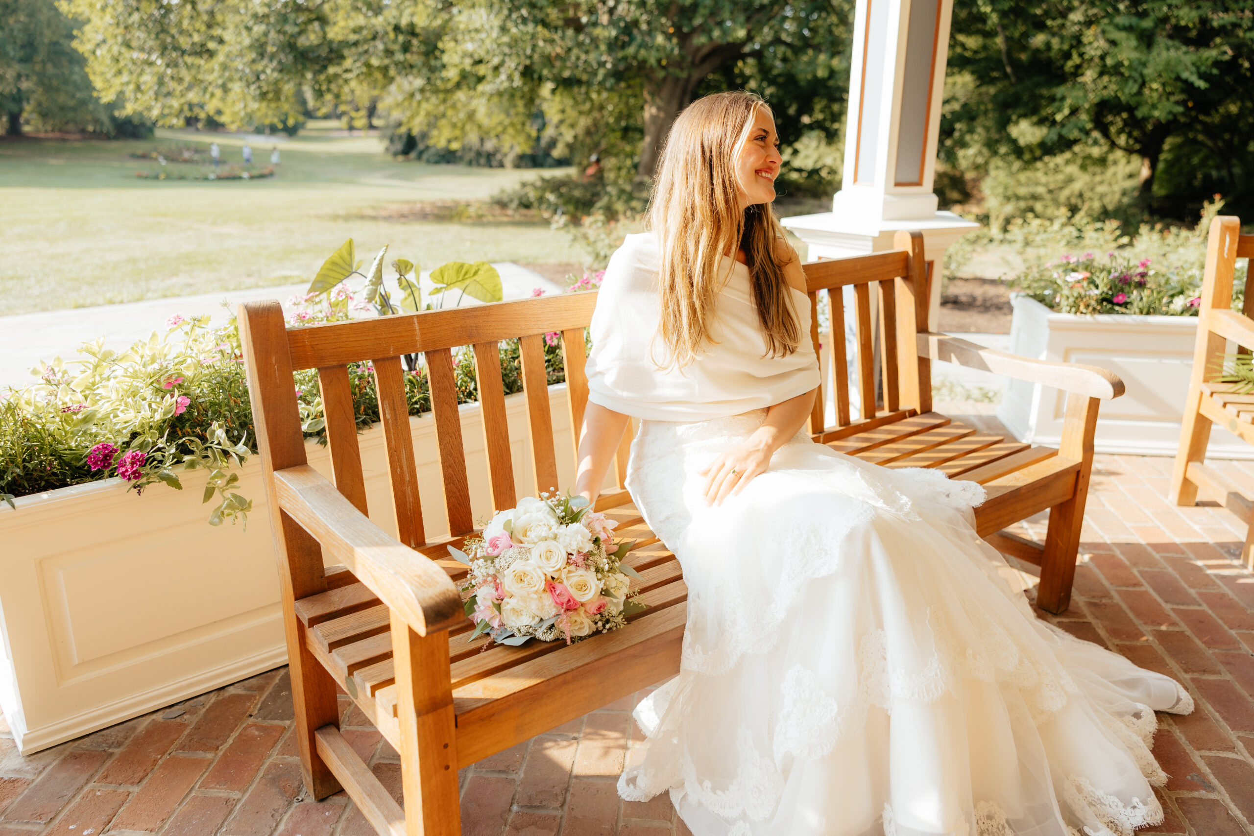 A bride sitting with her bouquet on a bench.