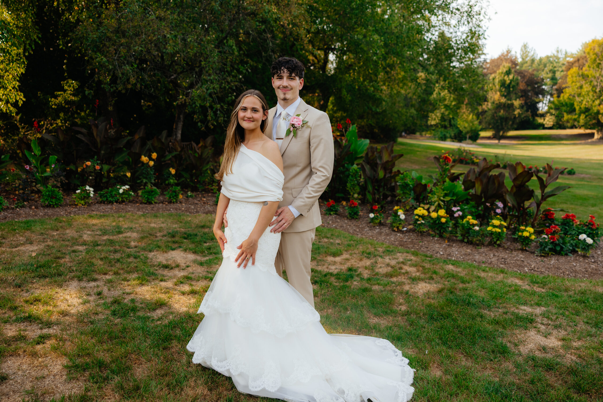 A bride and groom posing together with flowers at a park.