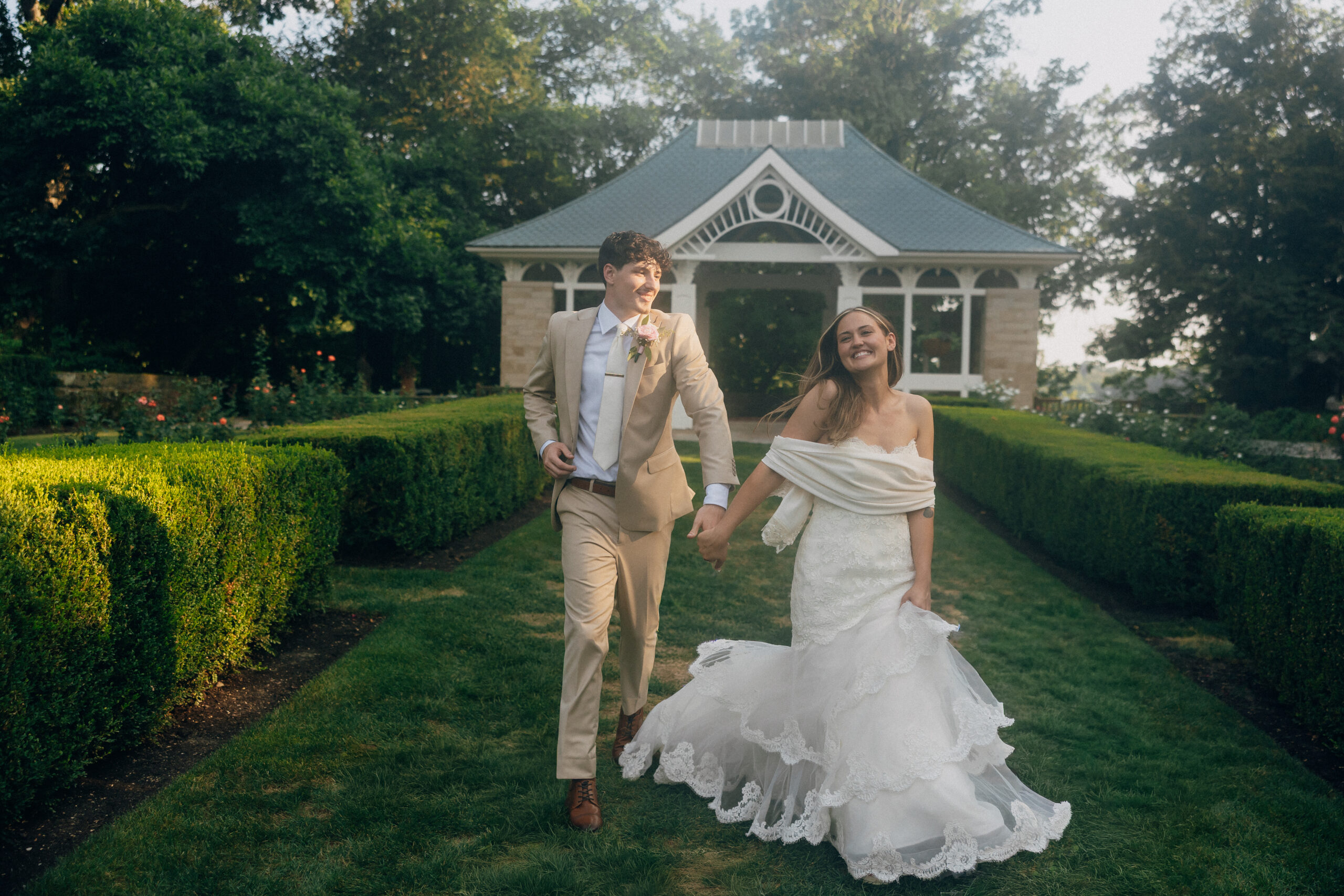 A bride and groom running in a garden holding hands.