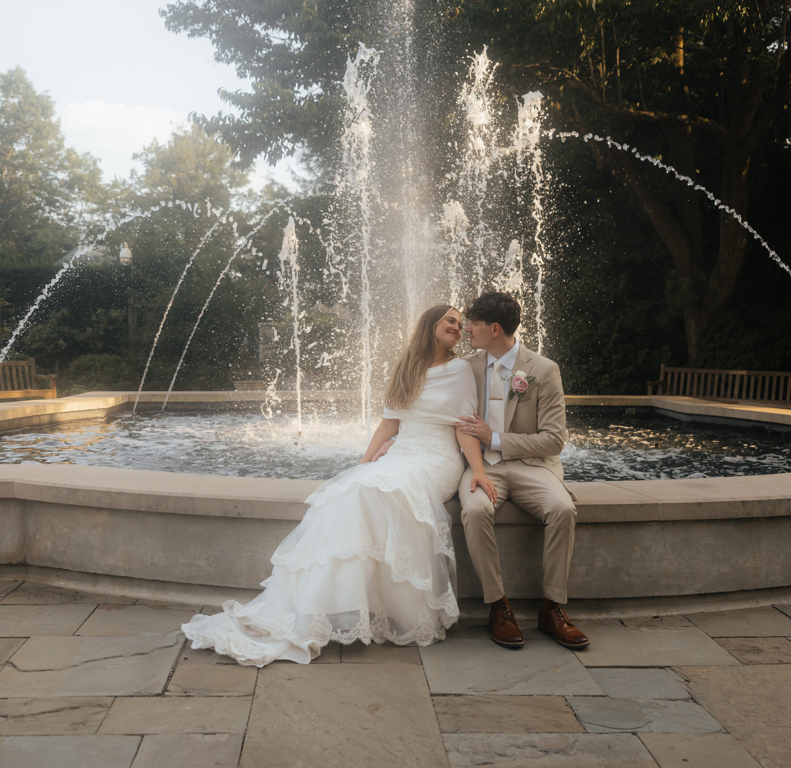 A bride and groom in front of a fountain.