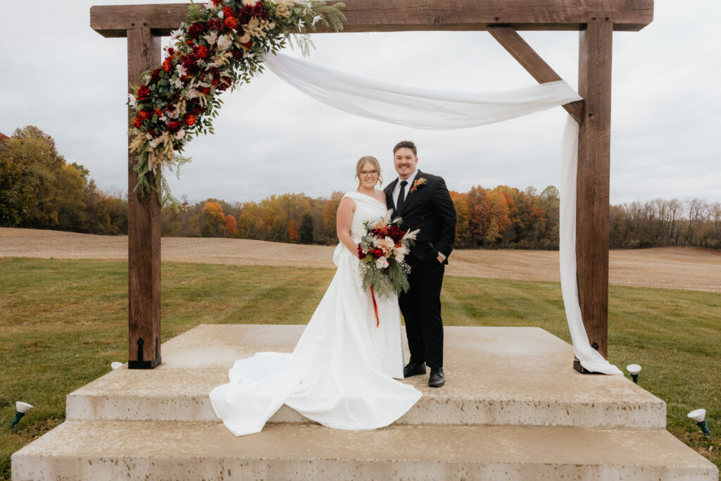 Bride and groom outside posed under a wooden arch.